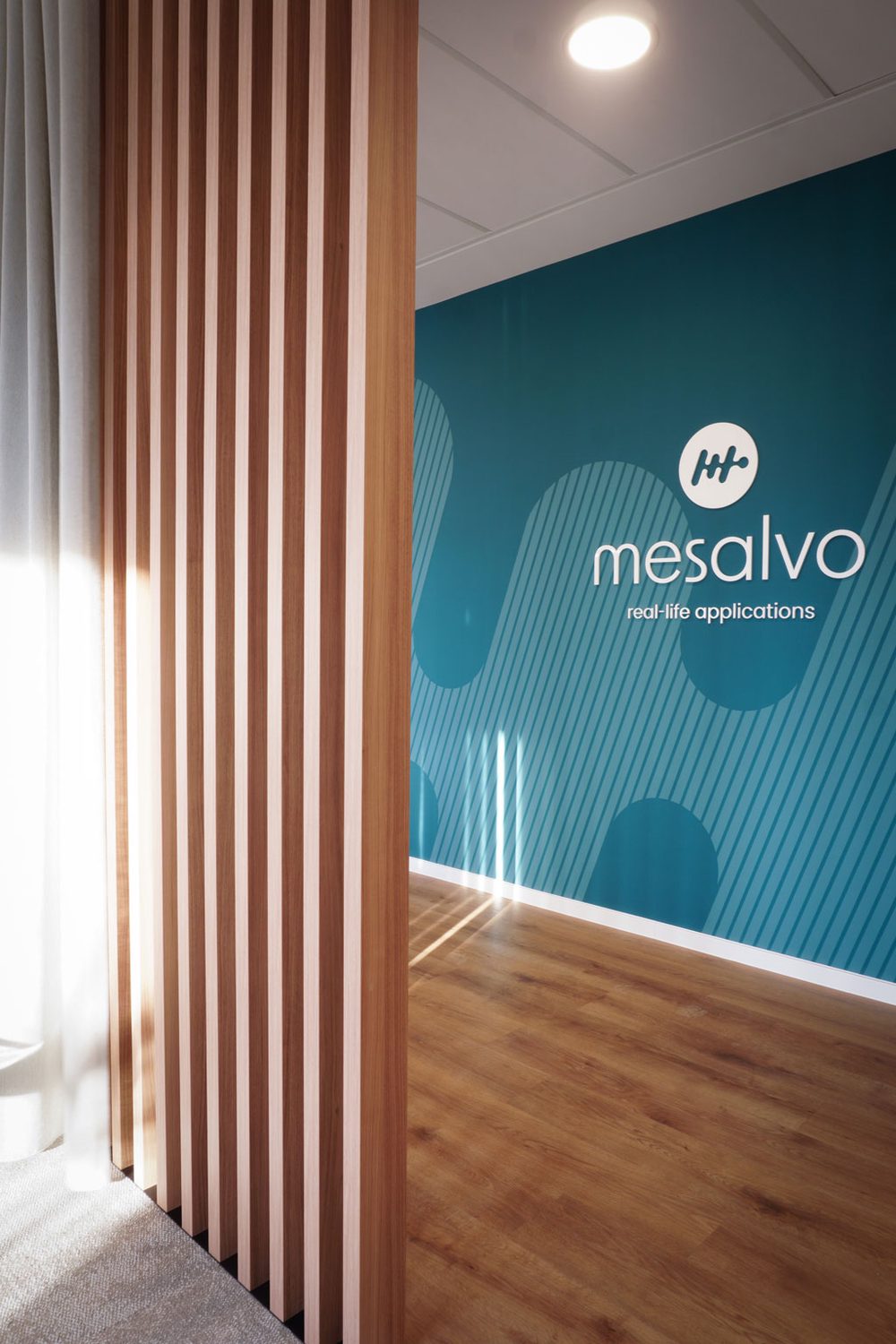 Markenwand in Türkis mit dem mesalvo-Logo, davor eine Reihe heller Holzlamellen