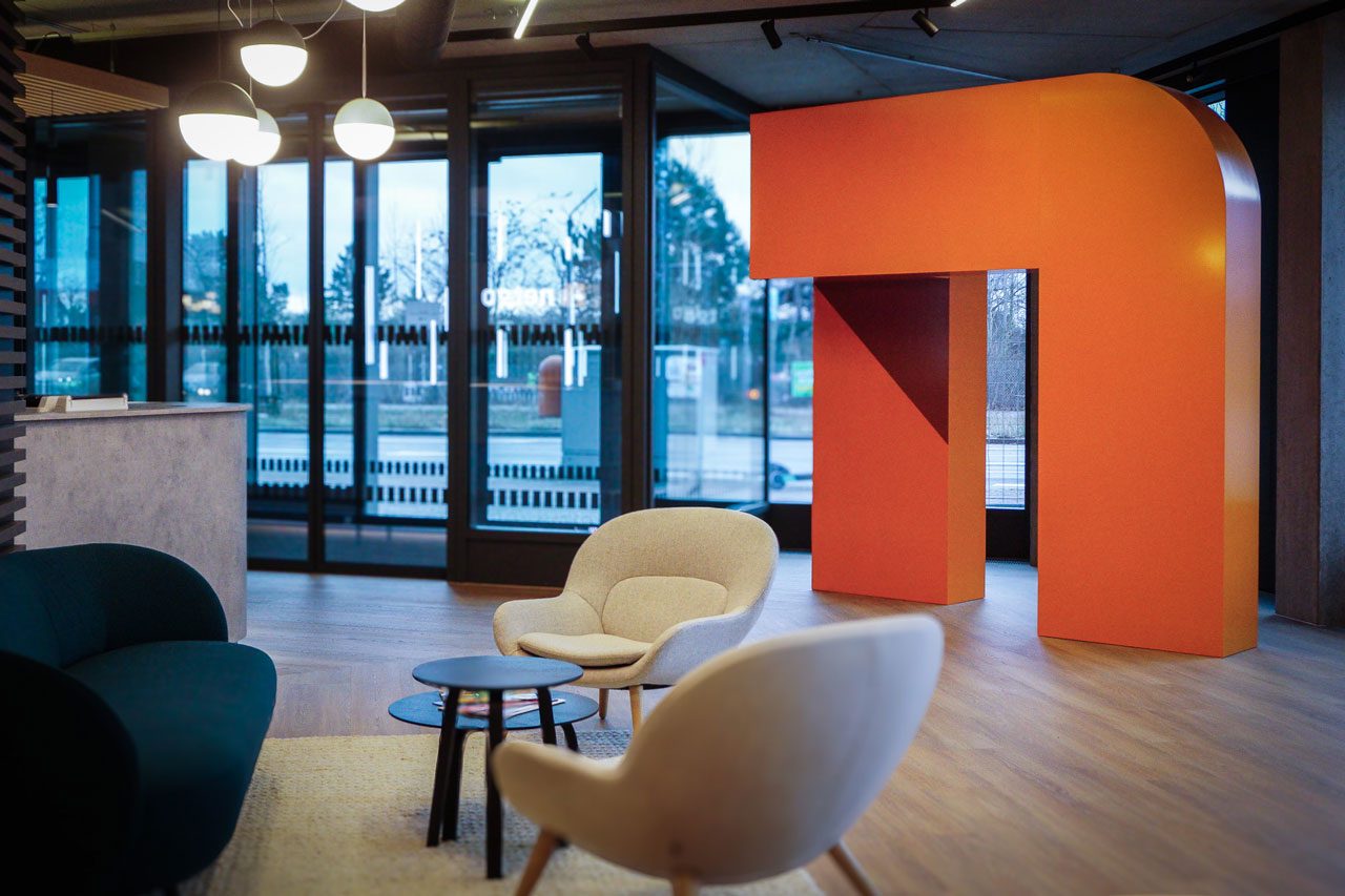 Loungebereich am Fenster mit Sesseln, Couchtisch und einer orangen Skulptur in Bogenform