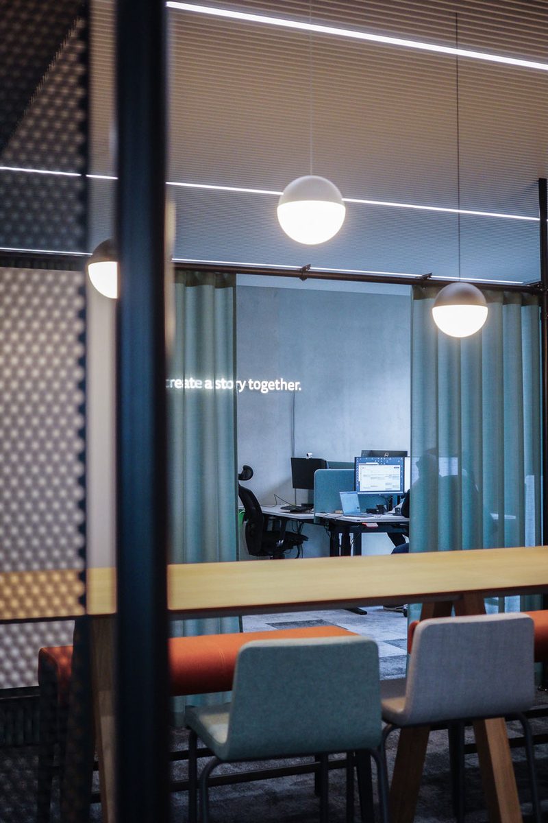 Arbeitsbereich hinter Glas und türkisem Vorhang, an der Wand der Schriftzug „Let’s grow together“