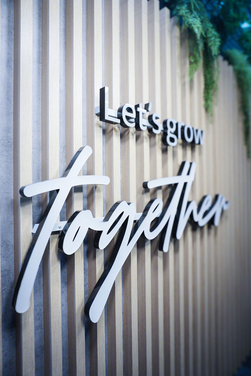 Schriftzug „Let’s grow Together“ in weißen Lettern auf einer Wand aus Holzlamellen