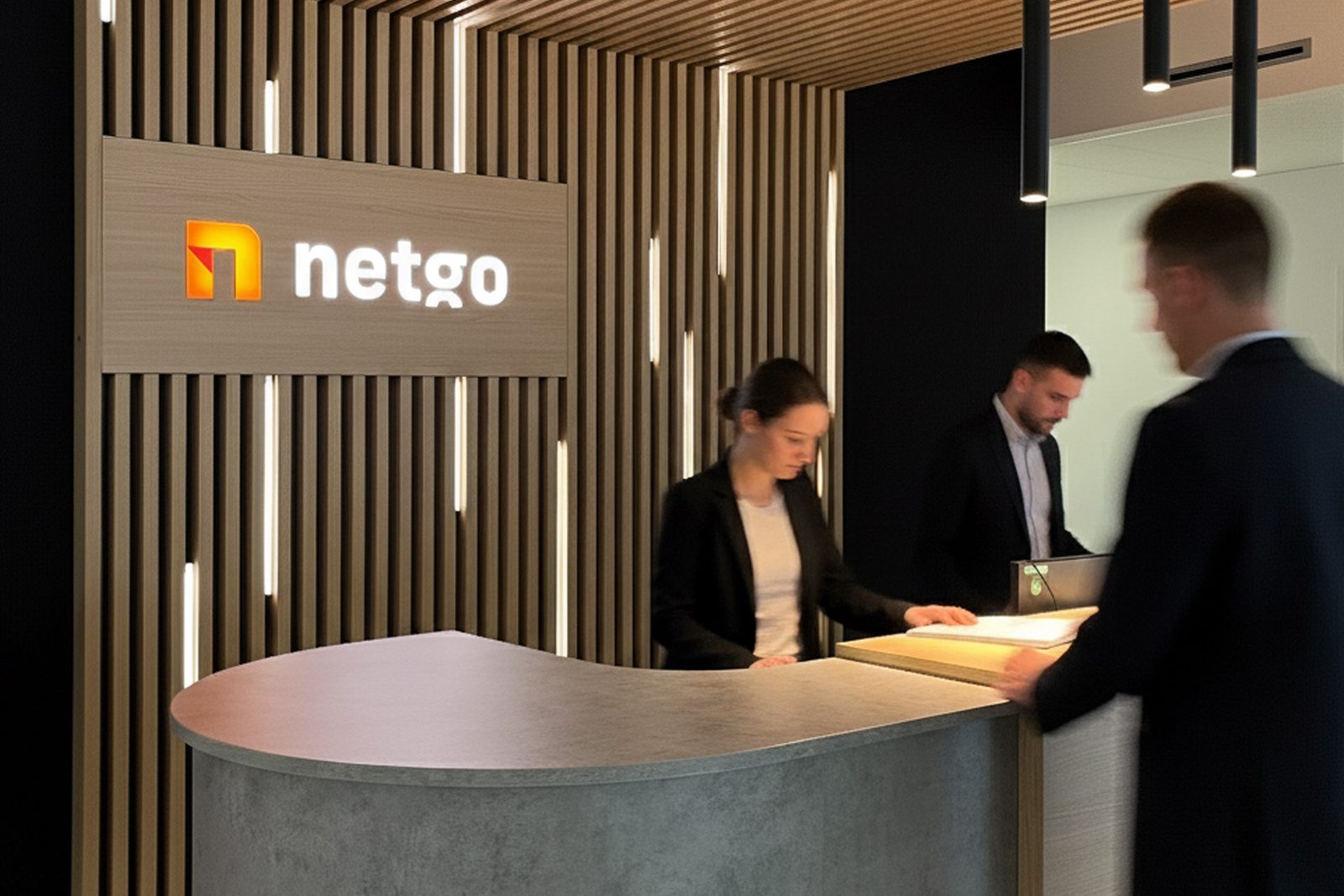 Empfang mit geschwungenem Tresen vor einer Wand aus Holzlamellen mit netgo-Logo, drei Personen im Gespräch