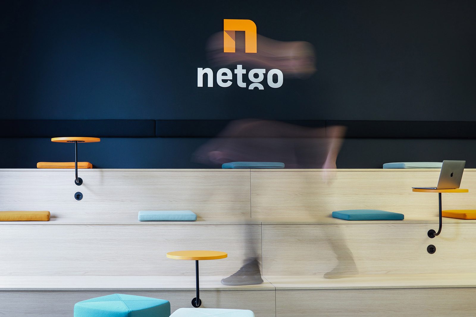 Arbeitsplätze mit orangen Hockern vor einer dunklen Wand mit großem netgo-Logo