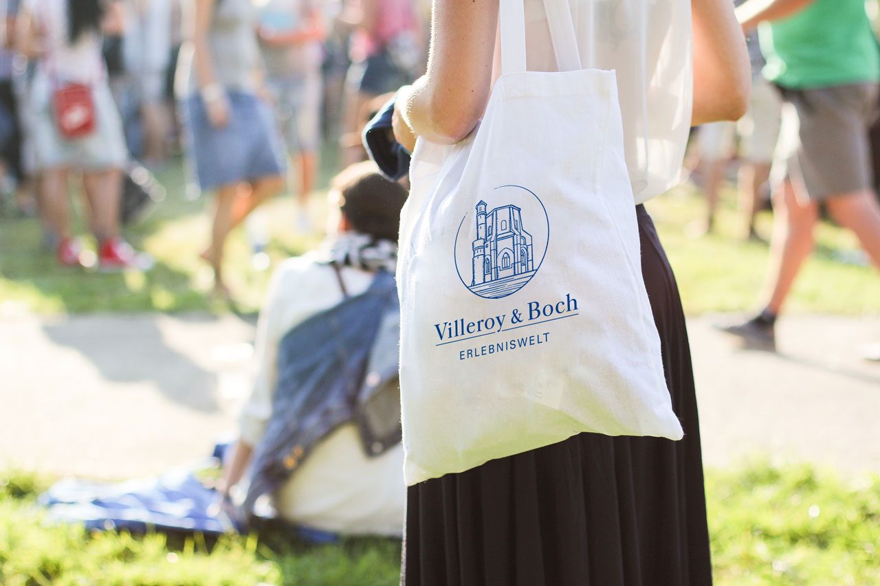 Person trägt eine Stofftasche mit dem Villeroy-&-Boch-Wappen über eine Wiese